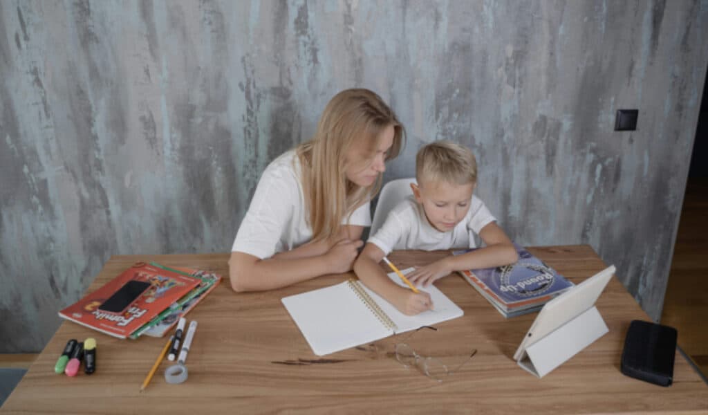 A woman and boy studying together with books and a tablet on a wooden table