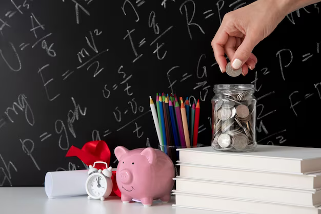 A hand throws coins into a jar next to textbooks, a piggy bank and pencils