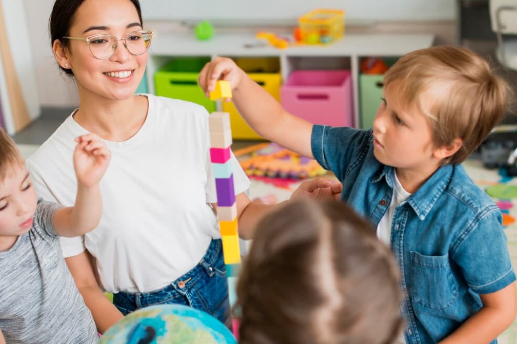 A teacher builds a colorful block tower with her preschool students