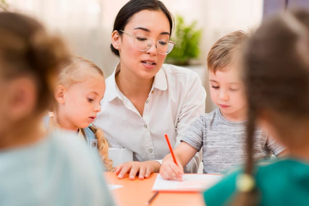 An educator guides a young boy and girl in a drawing lesson