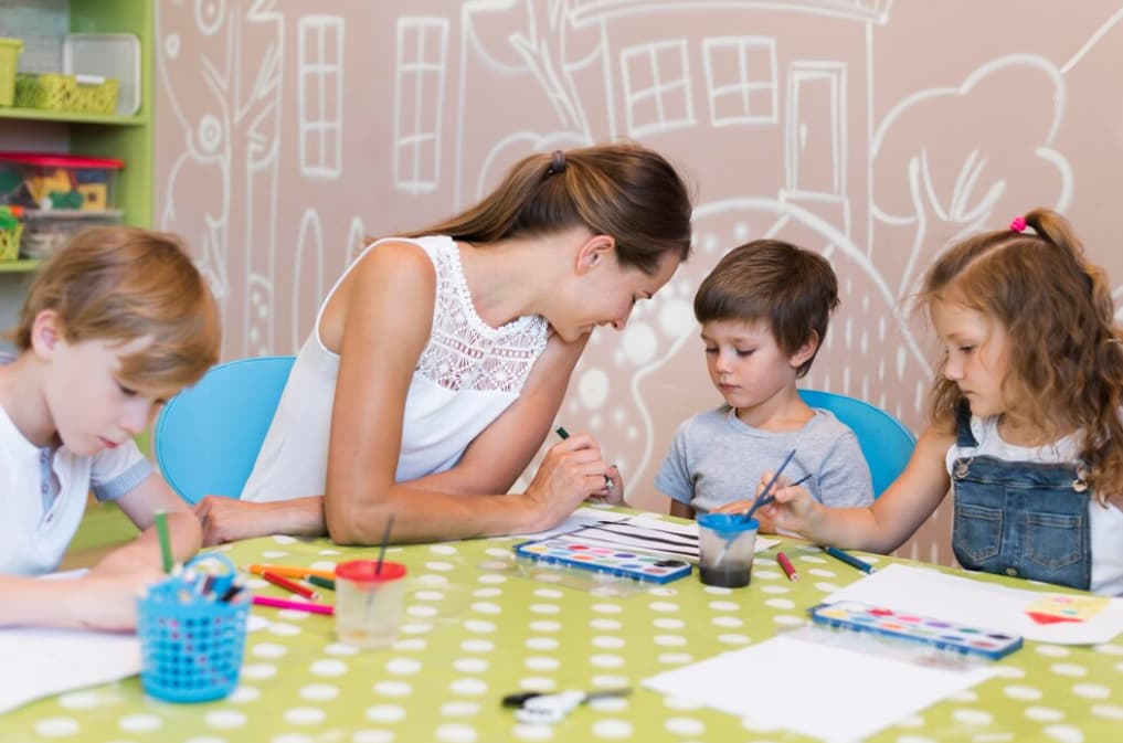 A teacher assists three kids with a watercolor painting activity